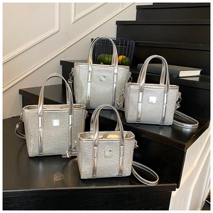 Detail view of silver sequined bucket bags in four sizes on black stairs with straps