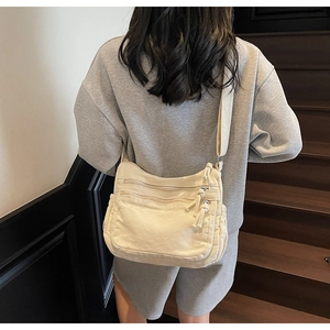 Detail view of a beige canvas crossbody bag with multiple zippers worn by a model