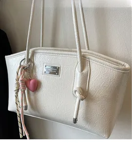 Detail view of cream white tote bag with textured faux leather and pink heart charm