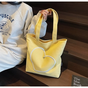 Détail d'un sac cabas en toile jaune vif avec une grande applique de cœur blanc et rivet en métal