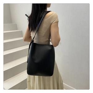 Minimalist black matte faux leather shoulder tote bag shown worn by a model in a modern setting