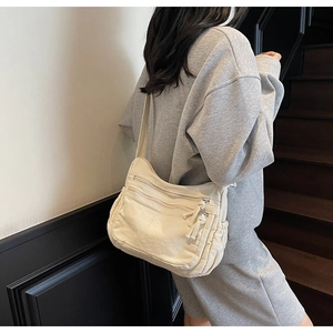 Detail of off-white canvas crossbody bag with multiple zippers and wide strap