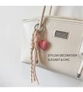 Close-up of pink heart charm with braided cords on white leather shoulder bag