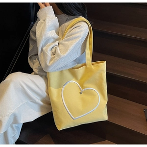 Sac cabas en toile jaune avec motif cœur, porté par un mannequin sur des marches