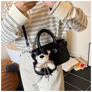 Détail du sac seau en similicuir croco noir avec une peluche de chiot blanc mignonne