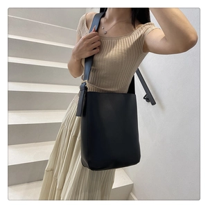 Close-up of a black minimalist bucket bag with a wide shoulder strap in a lifestyle setting