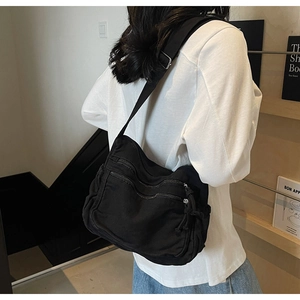 Detail of black canvas tote bag showing side drawstring and multiple zipper layers