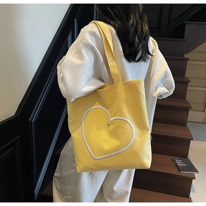 Détail d'un sac cabas en toile jaune avec contour de cœur sur un escalier en bois