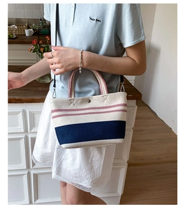 Detail of canvas bucket bag with red stripes and navy blue base on a female model