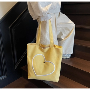 Détail d'un sac cabas en toile jaune avec cœur porté par un mannequin en escalier
