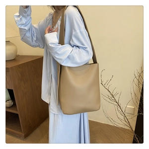 Minimalist khaki bucket bag with wide shoulder strap shown in a cozy interior scene