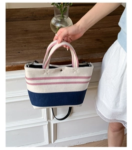 Detail of canvas tote bag with red stripes and blue paneling held by hand in casual setting