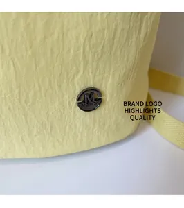 Detail shot of pale yellow wrinkled fabric and black metal logo badge on fashion tote