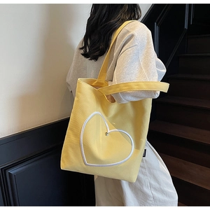 Détail du sac fourre-tout en toile jaune avec broderie coeur porté par un mannequin