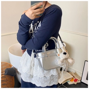 Détail du sac seau argenté avec pendentif chiot pelucheux et nœud sur la bandoulière réglable