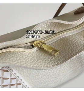 Detail of smooth gold zipper on beige pebbled leather tote bag with fabric accent