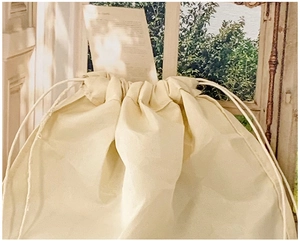Close-up of a beige cotton drawstring dust bag on a sunlit window sill with green plants