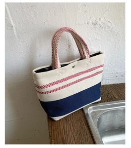 Close-up of a striped canvas tote bag featuring navy blue contrast bottom and red handles
