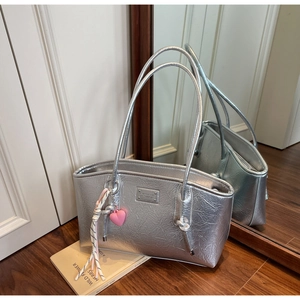 Detail of silver metallic tote bag featuring pink heart charm and polished brand plaque