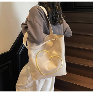 Détail d'un sac fourre-tout en toile minimaliste avec motif coeur doré porté par un mannequin