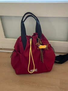 Deep red waterproof drawstring backpack with black handles and yellow dog charm accessory