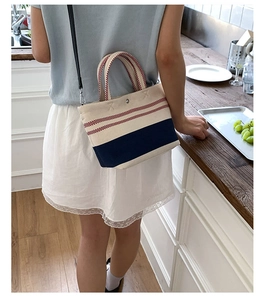 Detail of a striped canvas crossbody bag worn by a model in a bright, modern setting