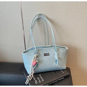 Detail of light blue pleated tote bag with silver plate and heart charm over books