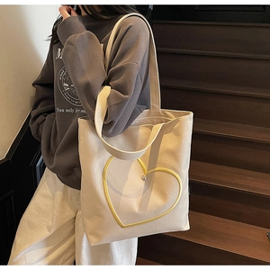 Détail du sac cabas en toile beige minimaliste avec contour cœur jaune porté à l'épaule