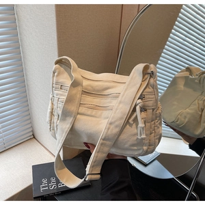 Close-up of cream canvas crossbody bag with multiple zippers and side drawstring pockets