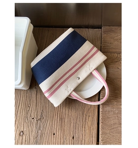 Close-up of beige canvas beach tote featuring navy stripe and red checkered handles