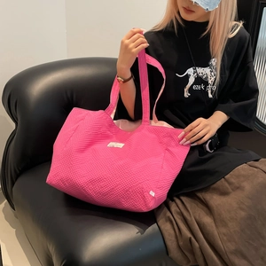 Détail du sac cabas rose fuchsia en tissu texturé tenu sur un canapé en cuir noir