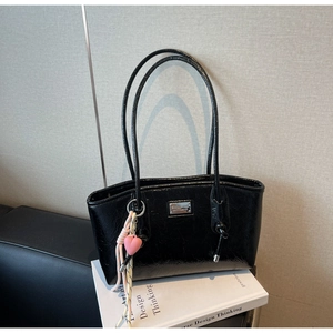 Detail of glossy black tote bag featuring a silver logo plate and pink heart charm