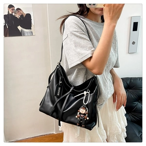 Detail of black leather tote bag featuring adjustable strap and astronaut doll pendant