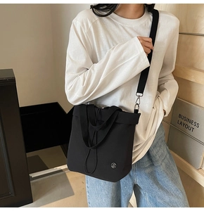 Detail of black canvas bucket bag with adjustable wide strap and circular metal M logo