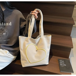 Détail du sac cabas en toile beige avec surpiqûres cœur jaunes sur escalier en bois