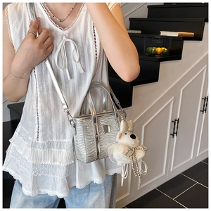 Silver glossy mini bucket bag with plush charm shown worn as a crossbody on a model