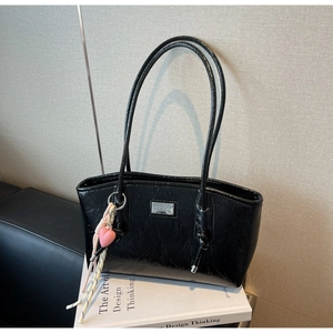 Detail of glossy black patent leather tote bag with silver logo and pink heart charm