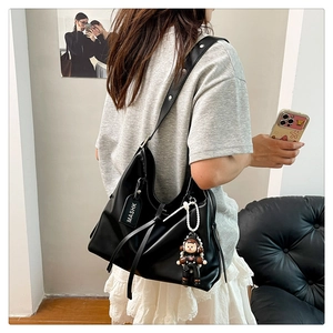Detail of black faux leather tote with silver studs, logo tag, and astronaut charm accessory