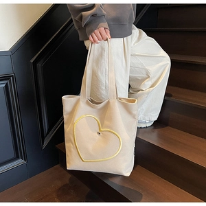 Détail d'un sac cabas en toile beige avec un motif cœur jaune sur l'escalier