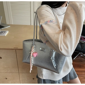 Detail of silver metallic tote bag featuring a pink heart pendant and tassel decoration