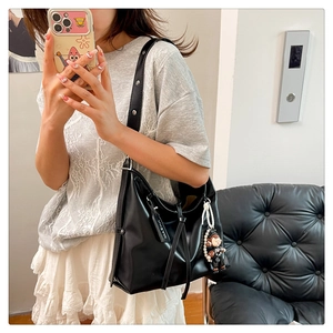 Detail of black large-capacity leather shoulder bag with decorative pearl chain charm