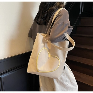 Détail du sac cabas en toile crème avec broderie cœur jaune porté par un modèle