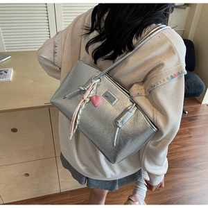 Detail of silver tote bag featuring pleated metallic texture and pink heart accessory