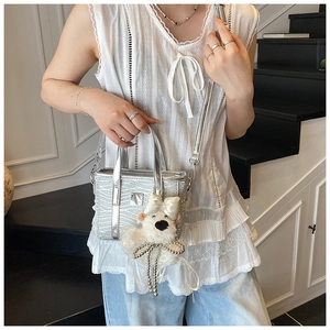 Detailed shot of silver textured tote bag featuring a cute teddy bear charm and pearl bow