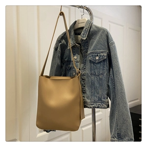 Detail view of khaki bucket bag hung on a hanger showing smooth texture and long strap