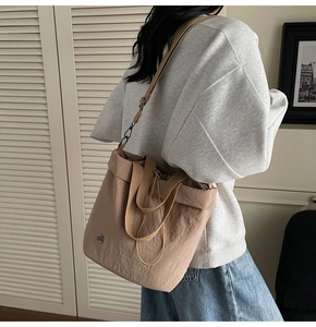Detail of light khaki drawstring tote bag with long strap and small metal logo