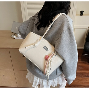 Close-up of cream tote bag with natural pleats, metal logo plate and heart pendant