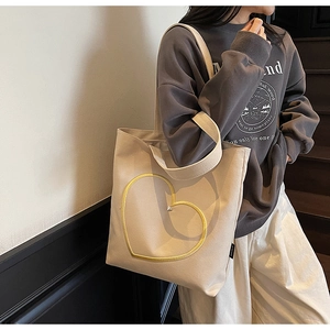 Détail du sac cabas en toile crème avec broderie coeur jaune porté à l'épaule