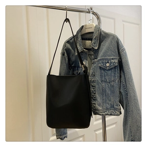 Detailed side view of a black leather bucket bag paired with a blue denim jacket