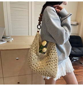 Detail of hollow-out woven shoulder bag with dark brown wooden beaded strap on a wooden desk